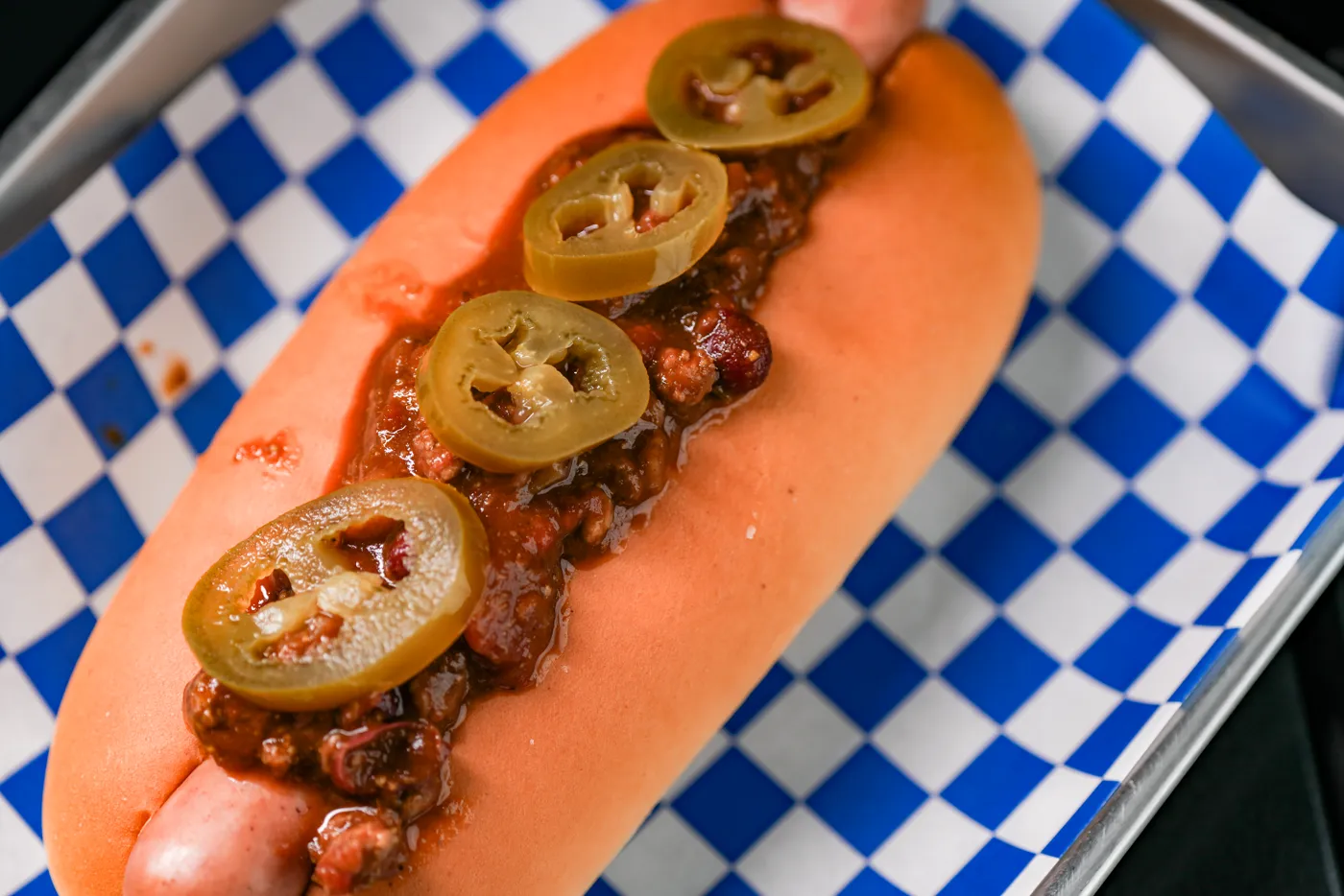 藍白格紋紙上的 Hotdogray 熱狗，香腸淋上肉醬，鋪著幾片墨西哥辣椒